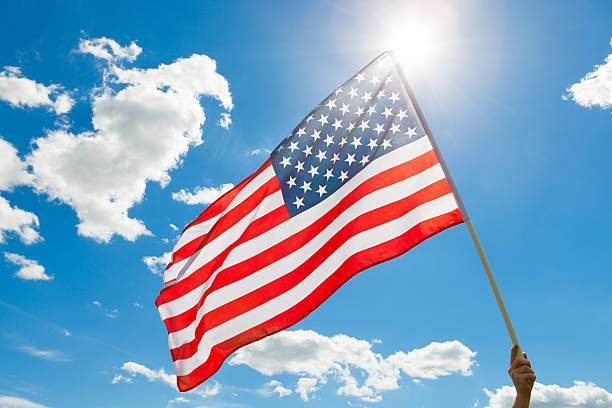 istock American flag waving in blue sky with sun behind it 539079785