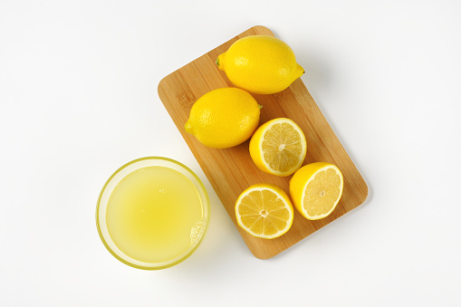 bowl of freshly squeezed lemon juice and ripe lemons on wooden cutting board