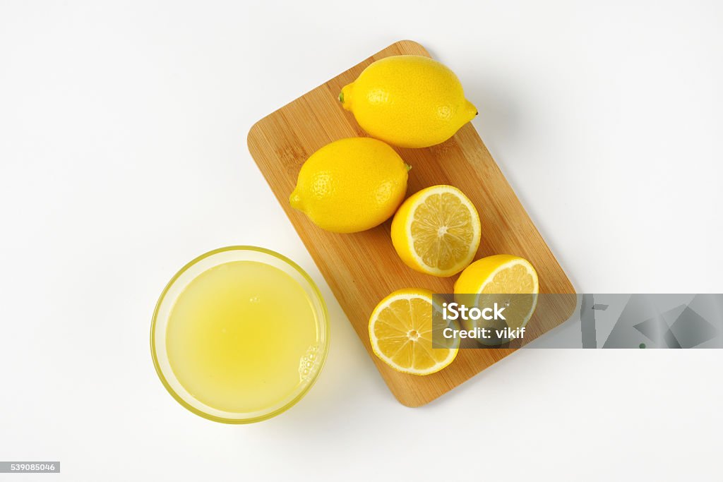 lemon juice and fresh lemons bowl of freshly squeezed lemon juice and ripe lemons on wooden cutting board Lemon Juice Stock Photo