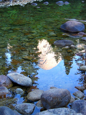 Reflection of North Done in the rock strewn bed of Merced river in Yosemite National Park