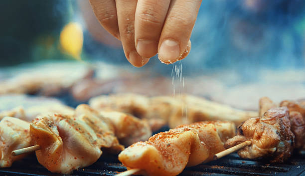 Chef seasoning meat on a grill. Closeup of unrecognizable male chef seasoning meat on a grill with a pinch of salt. Very shallow focus. salt seasoning stock pictures, royalty-free photos & images
