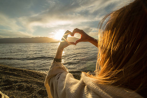 Young woman by the lake making heart shape finger frame Young woman by the lake making a heart shape finger frame. Lake and mountain landscape. hands forming heart shape stock pictures, royalty-free photos & images