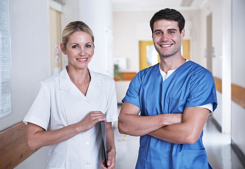 Portrait of two healthcare workers standing in a hospital corridor with a medical chart