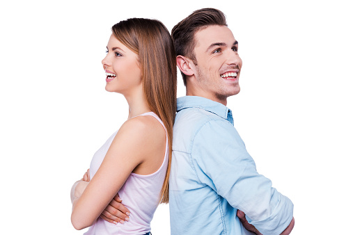 Beautiful young loving couple smiling and standing back to back against white background