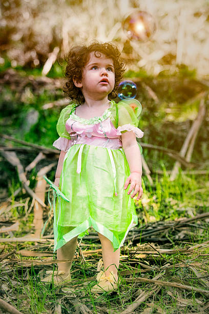 little girl in forest dressed as a fairy looking at a light