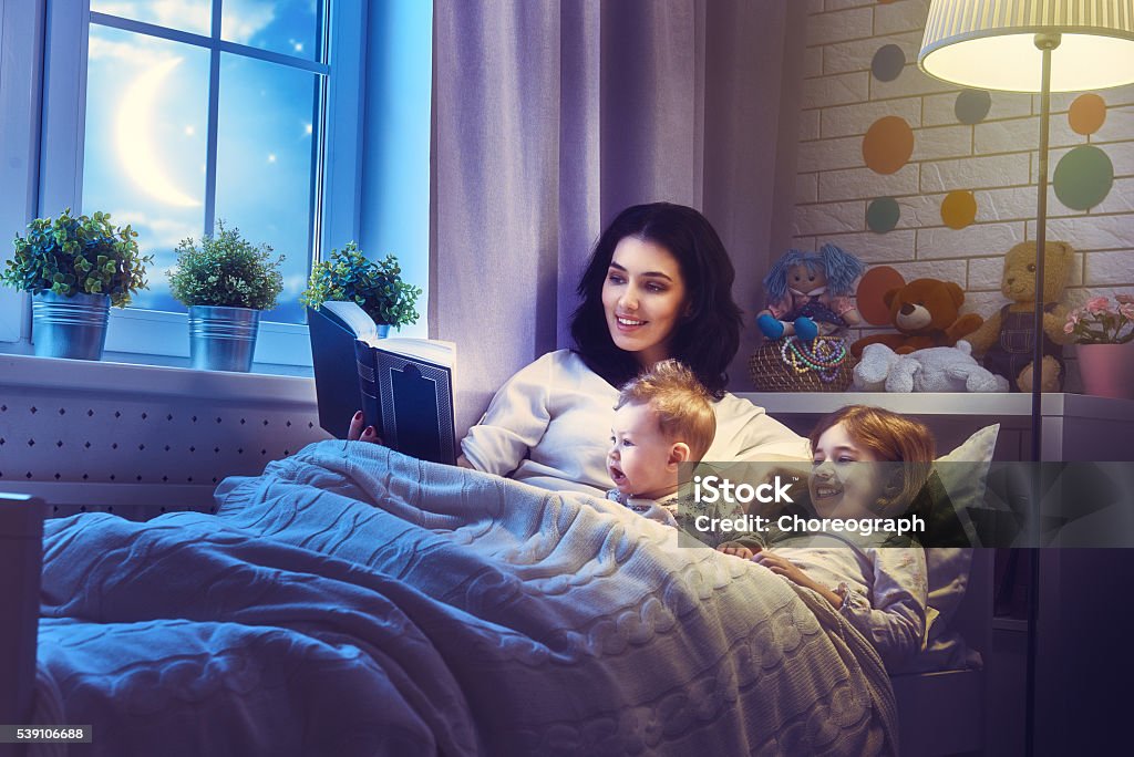 mother reading a book Family reading bedtime. Pretty young mother reading a book to her daughters. Storytelling Stock Photo