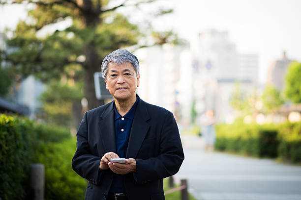 Senior Japanese man using a smart phone Senior Japanese man using a smart phone in an urban setting 60 69 years stock pictures, royalty-free photos & images
