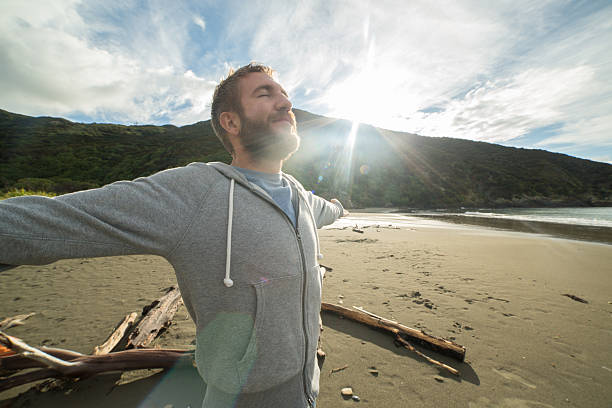 Cheering young man arms outstretched on the beach at sunrise.