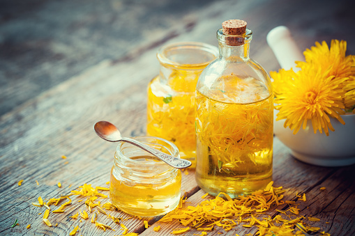 Dandelion tincture or oil bottles, mortar and honey on table. Herbal medicine.