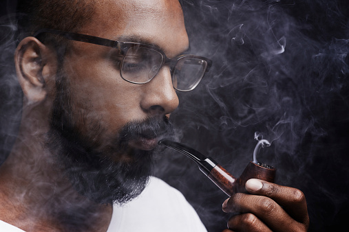 Cropped shot of a young man smoking a pipe in the studio