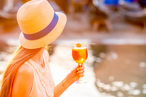 Young woman with glass of Spritz Aperol sitting near the water chanal in Venice on the sunset. Traditional italian appetizer drink. Image with small depth of field