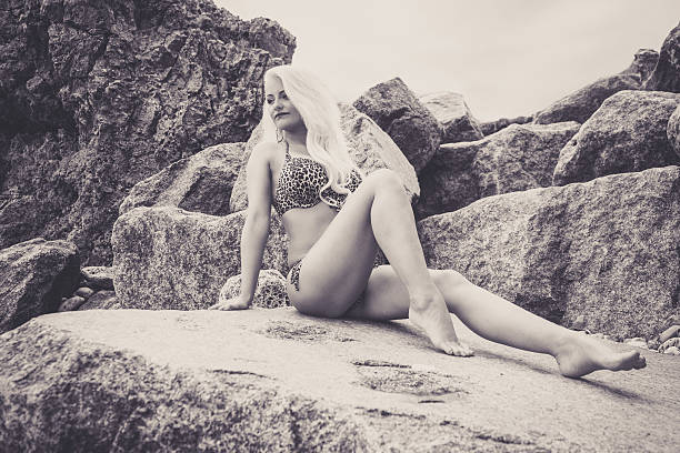 Beautiful young blonde haired woman sat on the rocks stock photo