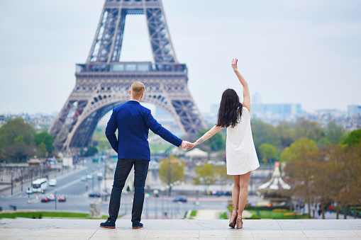 Young mixed race military couple on honeymoon in Paris. The American man is wearing a sailor uniform while his Indian wife in wearing a ceremonial white dress. Eiffel tower in the background. Monochrome black and white image with slightly grainy finish.