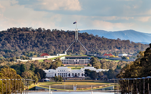 Close-up view of Canberra Capitol hill with New and Old Parliament houses on a line from ANZAC parade across Burley Griffin lake. Eucalyptus hills rising behind the city.