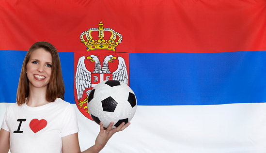 Attractive female soccer fan with textile flag of Serbia seamless close up with wind waves in the real fabric