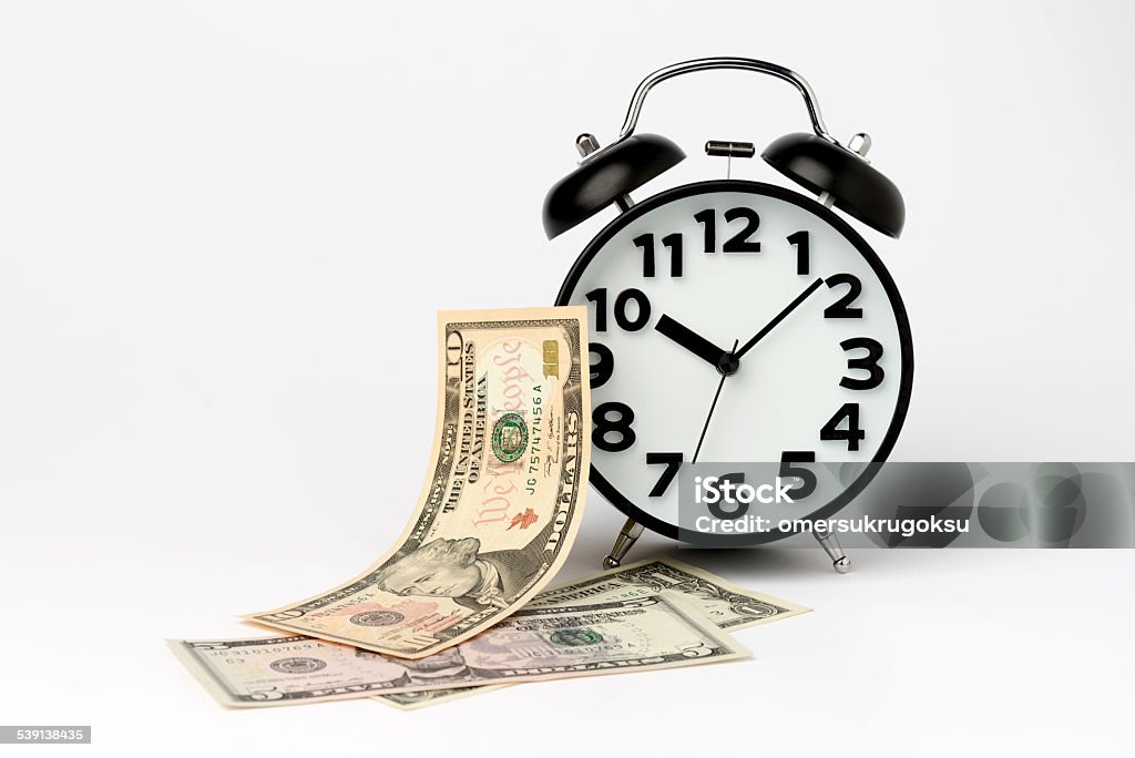 Black Table Clock with US Dollar on White Background Classic alarm clock with US Paper Currency isolated on white background. American Ten Dollar Bill Stock Photo