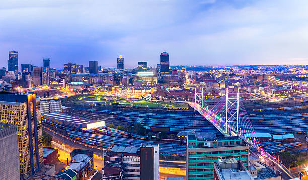 Nelson Mandela Bridge in the evening with Johannesburg Nelson Mandela Bridge panoramic (three pics) seen in the evening sunset with multicoloured lighting cityscape of Johannesburg city. johannesburg photos stock pictures, royalty-free photos & images