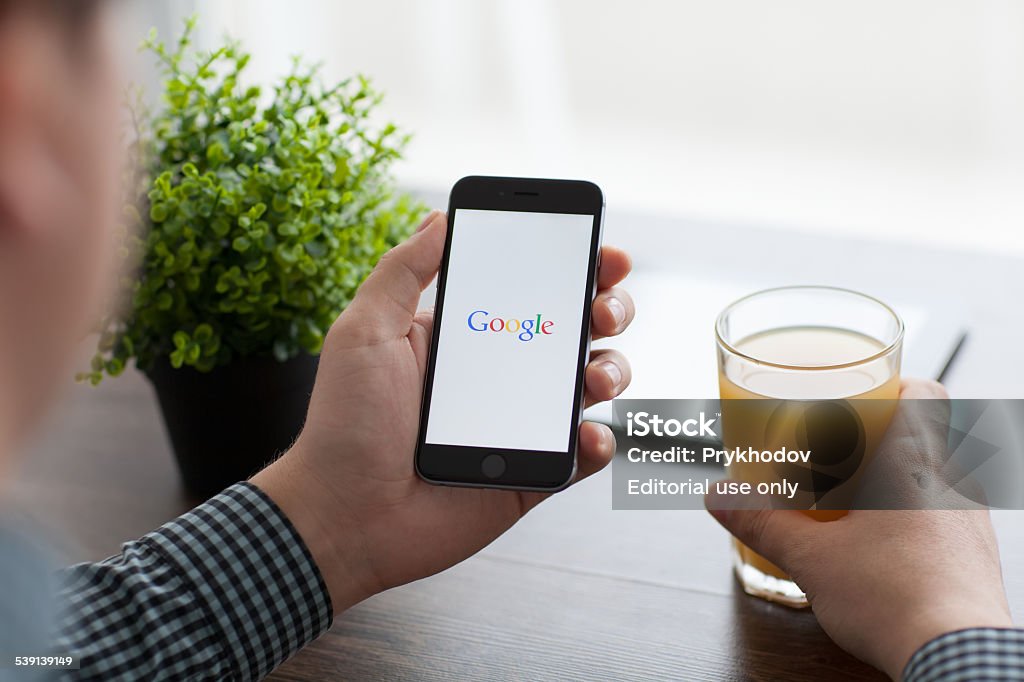 Man holding iPhone 6 with Google on the screen Alushta, Russia - November 21, 2014: Man holding a iPhone 6 Space Gray with social networking service Google on the screen. iPhone 6 was created and developed by the Apple inc. Searching Stock Photo