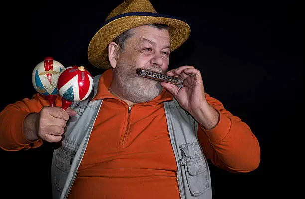 Senior musician with mouth-organ and maraca playing on a stage