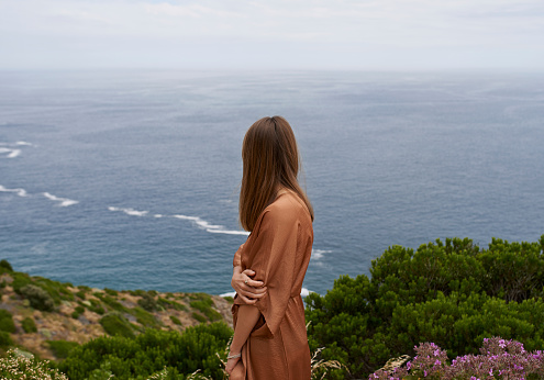 Shot of an attractive woman standing on a mountain looking out at the ocean