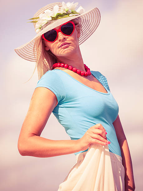 Fashion, happiness and lifestyle concept. Lovely blonde girl in hat and color sunglasses walking on beach. Young woman relaxing on the sea coast.