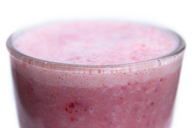 Photo showing a healthy strawberry smoothie / milkshake drink, served in an American diner-style tumbler glass.  This drink has been made for breakfast as part of a healthy eating, diet programme.  As well as containing blended frozen strawberries, milk and yoghurt / yogurt, the smoothie also features carrots, porridge oats, nuts (for added protein) and a banana.