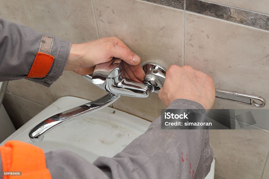 Plumber fixing faucet in a bathroom Plumber hands fixing water  tap with spanner 2015 Stock Photo