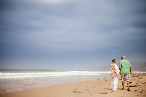 Senior African American couple walking on the beach, running from the waves