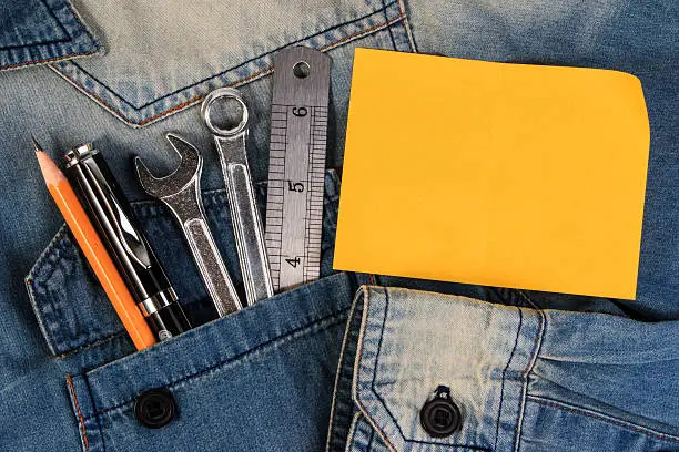 Photo of Wrench tools on a denim workers with blank note paper.
