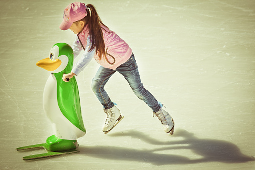Adorable little girl in winter clothes and hat skating on ice rink at Canada