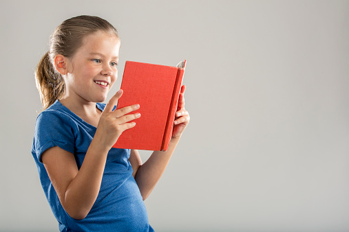 A young girl in blue reading a red book (with copy space to the right)