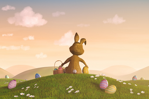 A cute Easter bunny sitting on a hill surrounded by easter eggs.