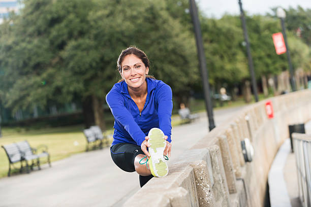 Middle aged woman stretching after a jog in the park Mature woman exercising, staying in shape by running, taking a break to stretch. one mature woman only stock pictures, royalty-free photos & images