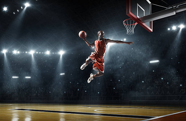 Basketball player makes slam dunk Close up image of professional basketball player about to do slam dunk during basketball game in floodlight basketball court basketball player photos stock pictures, royalty-free photos & images