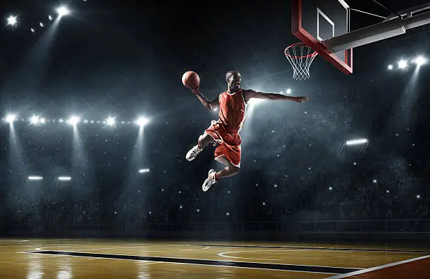 Close up image of professional basketball player about to do slam dunk during basketball game in floodlight basketball court