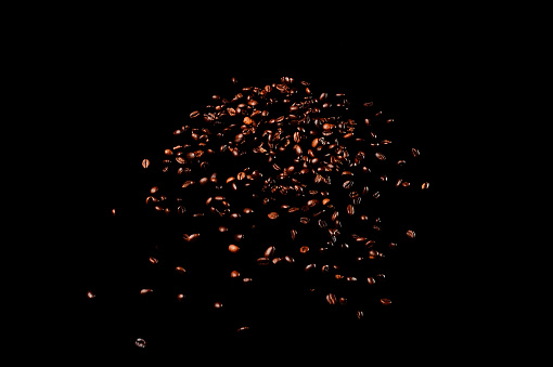 Flying coffee beans isolated on black background. Roasted coffee grains explosion.