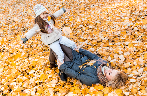 Happy mother lying in the leaves and having fun with her little girl during autumn day. 