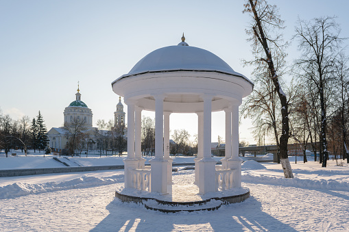 White arbor with the columns, standing on the shore of frozen river in winter.