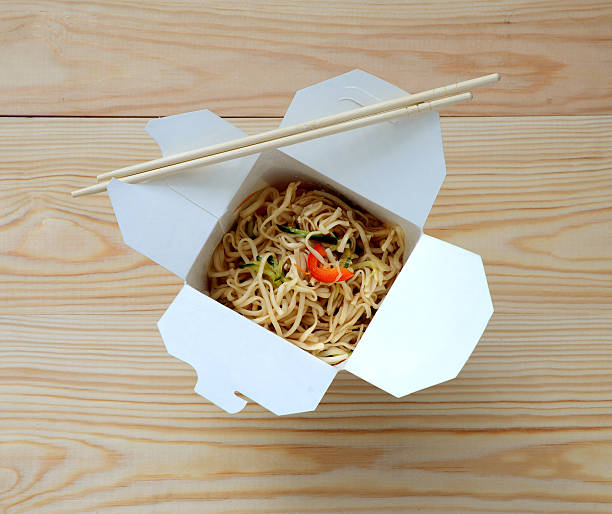 Chinese noodles in takeaway box on wooden background.