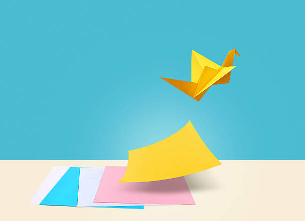 Creative Idea There are four colorful papers on a table with a blue background. Yellow paper is the symbol for creative ideas which is separating itself from other papers by flying like a bird. origami stock pictures, royalty-free photos & images