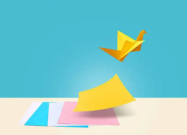There are four colorful papers on a table with a blue background. Yellow paper is the symbol for creative ideas which is separating itself from other papers by flying like a bird.