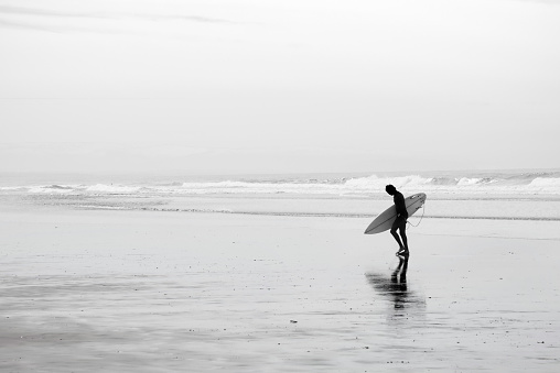 An image of the silhouette of a surfer leaving the ocean on a winter morning in Pismo Beach, California.
