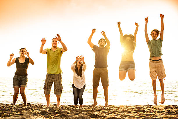 group of happy young people dancing at the beach on  beautiful summer day