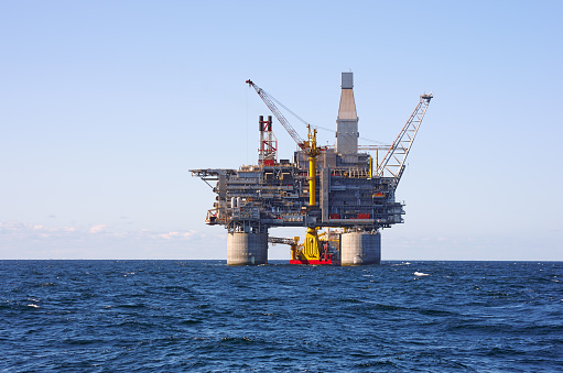 Oil rig and support vessel on offshore area. Blue sky background.