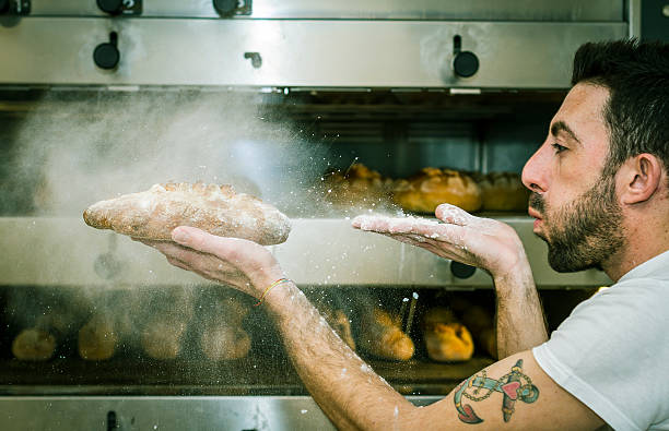 Young man (baker) blows the flour on bread