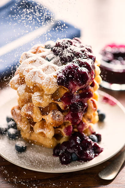 Belgium Waffles Stack, Blueberry Compote, Fresh Blueberries and Icing Sugar A sprinkling of powdered sugar is added as a final touch on a stack of Belgium waffles with homemade blueberry compote, fresh blueberries. sprinkling powdered sugar stock pictures, royalty-free photos & images