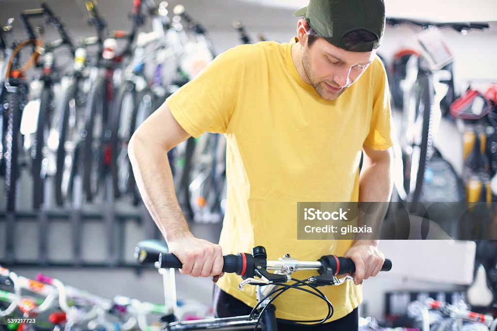 Bike mechanic at work. Early 30's bike mechanic checking suspension and brakes on customer's bike. Wearing yellow shirt and backwards pointed baseball cap. 2015 Stock Photo