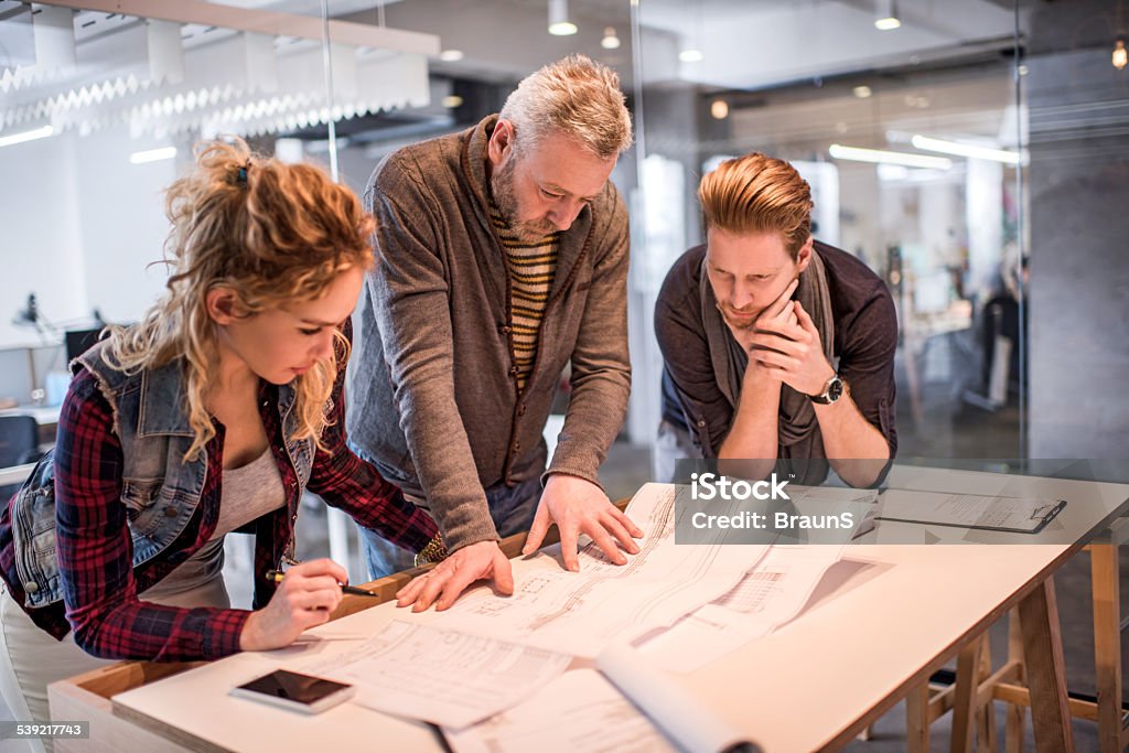 Architects planning a new project. Three creative people working together on blueprints. Architect Stock Photo