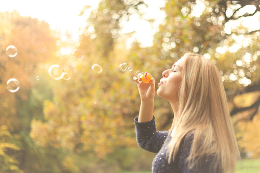 Woman enjoying the autumn sun outdoors in sunset, blowing soap bubbles.