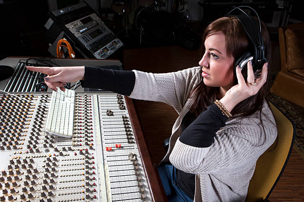 Female sound engineer at studio mixing desk Female sound engineer at studio mixing desk, pointing in direction of the performing artists sound technician stock pictures, royalty-free photos & images